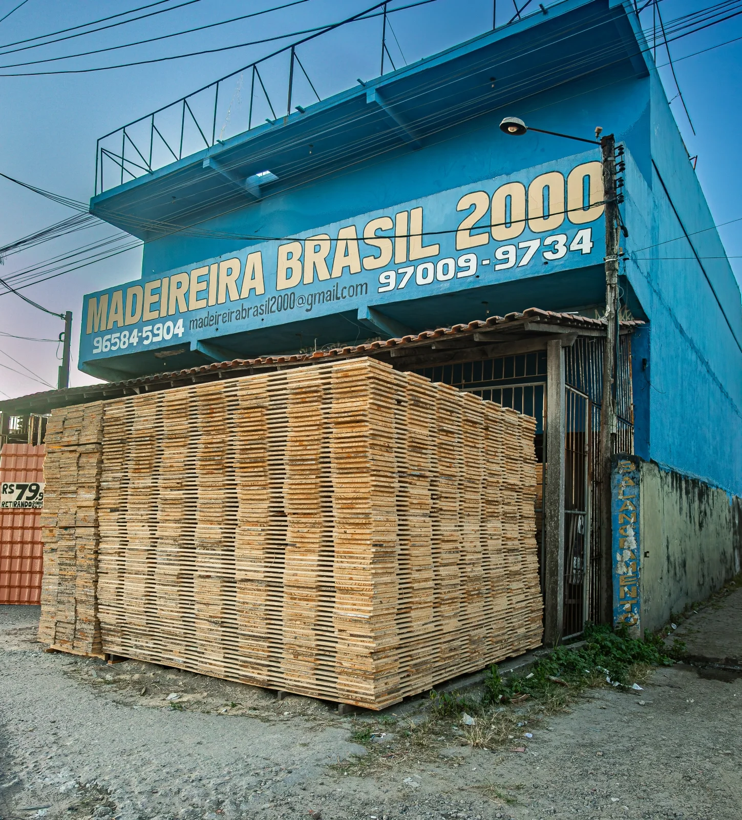 Fachada azul da Madeireira Brasil 2000, com tábuas de madeira à entrada